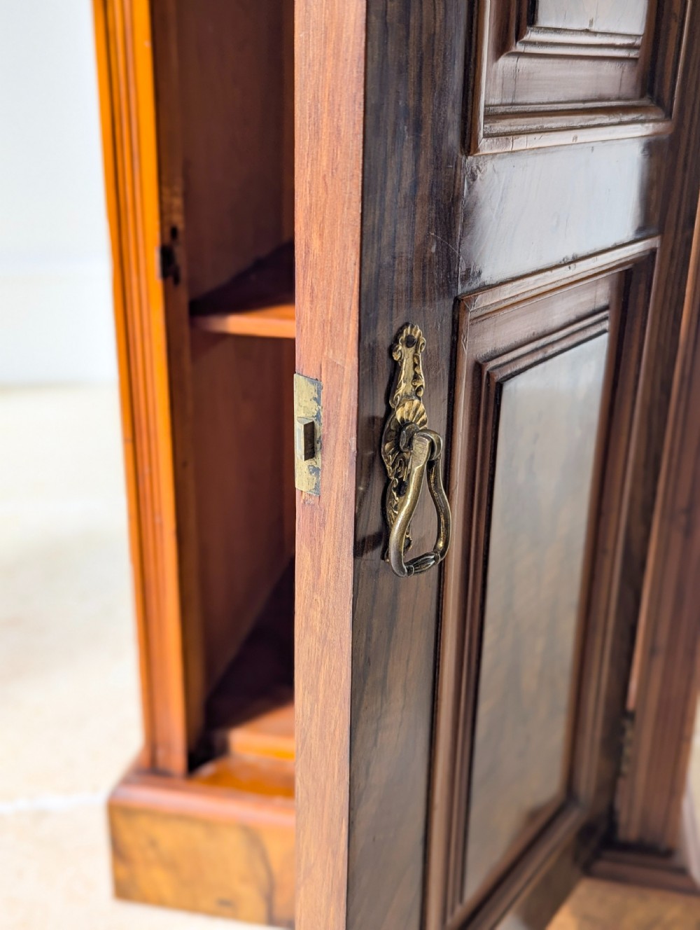 A late Victorian mahogany and exotic wood bedside cupboard featuring a carved top gallery, panelled door with brass drop handle, and a solid plinth base. View VIII