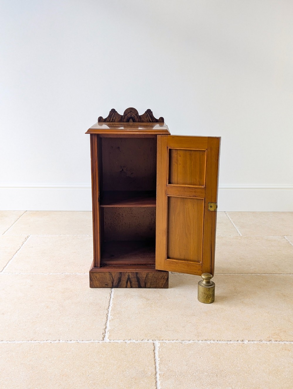 A late Victorian mahogany and exotic wood bedside cupboard featuring a carved top gallery, panelled door with brass drop handle, and a solid plinth base. View IX