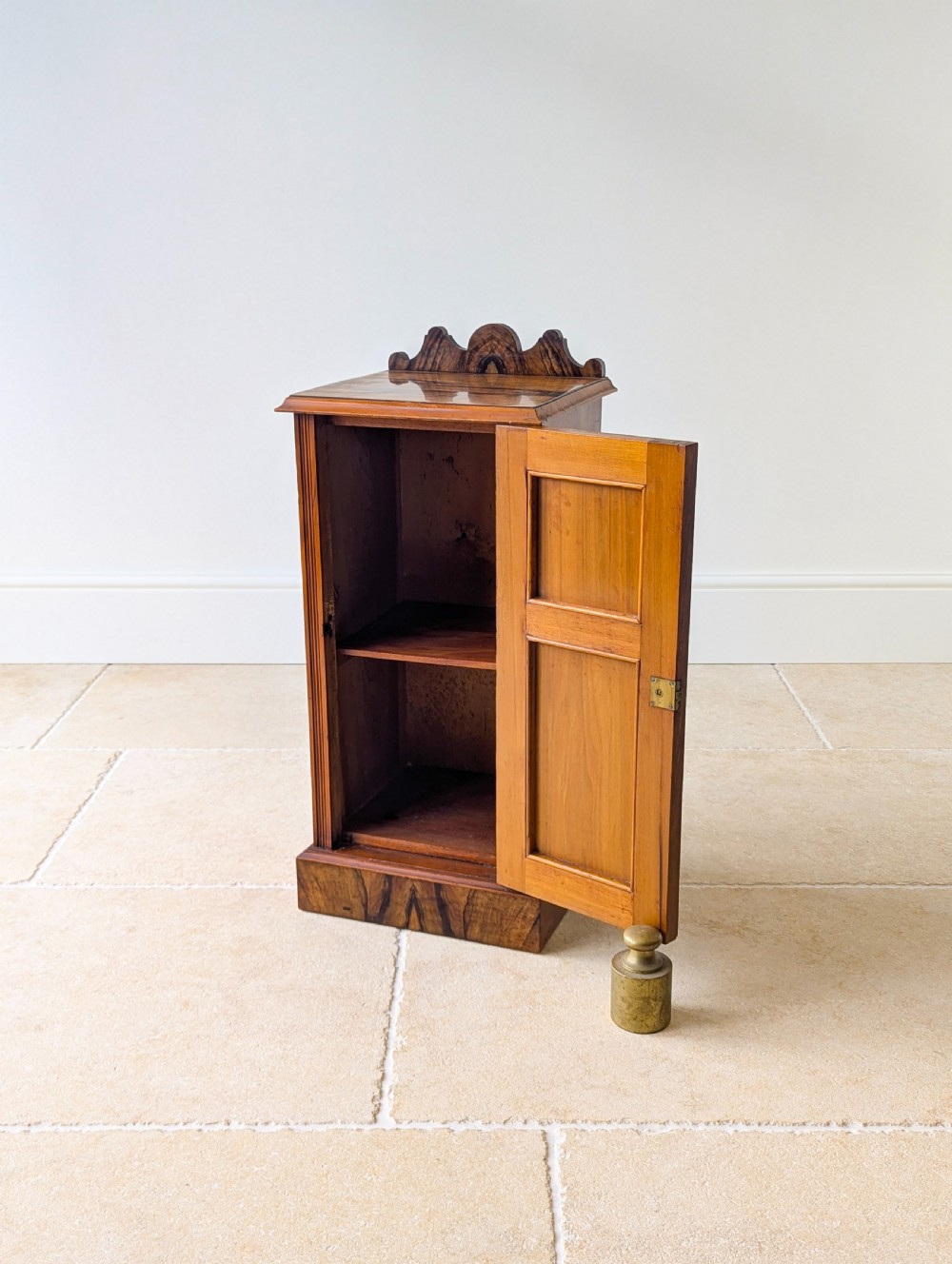 A late Victorian mahogany and exotic wood bedside cupboard featuring a carved top gallery, panelled door with brass drop handle, and a solid plinth base. View XIII