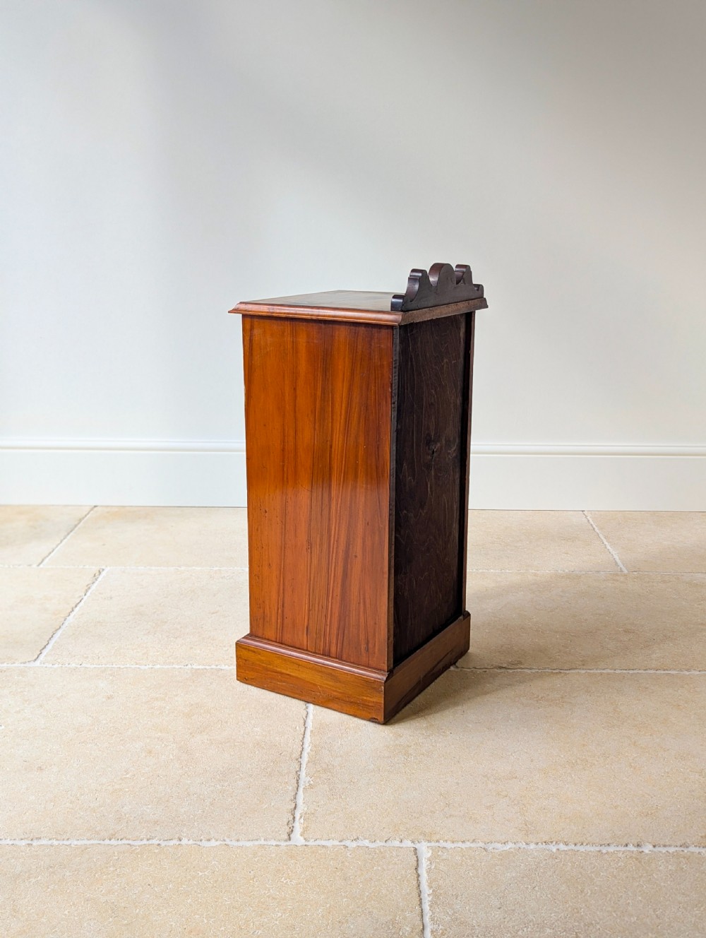 A late Victorian mahogany and exotic wood bedside cupboard featuring a carved top gallery, panelled door with brass drop handle, and a solid plinth base. View XVI