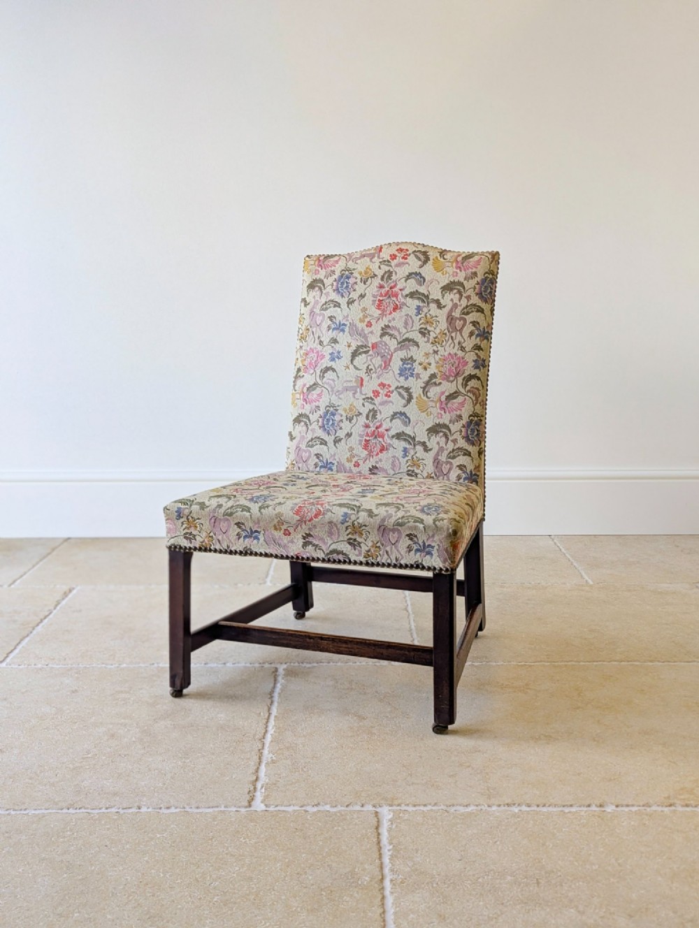 A mid-19th century Victorian side chair with dark mahogany legs on brass castors and dense floral upholstery framed with brass studding.