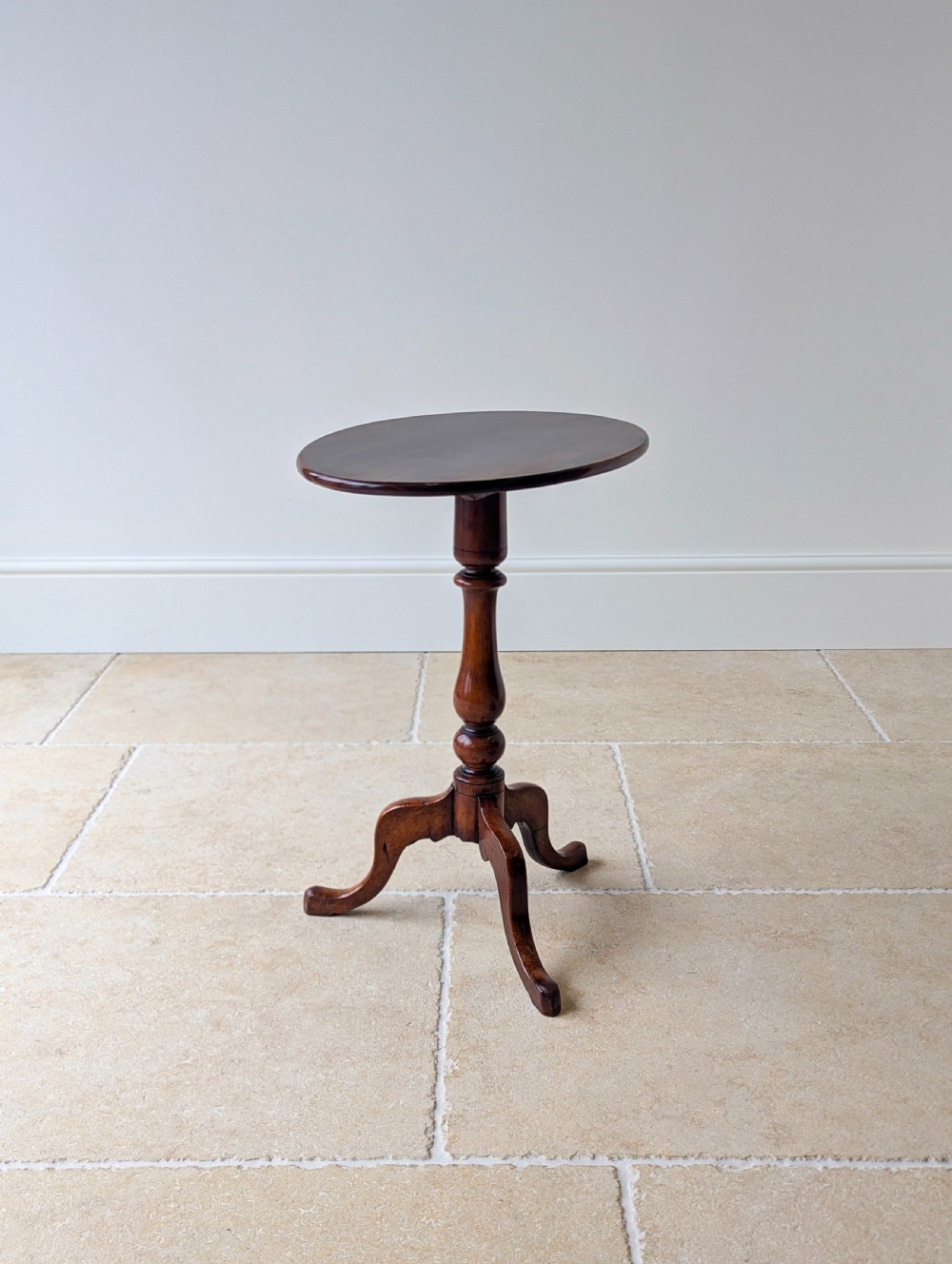 An antique Georgian mahogany wine table featuring a smooth oval top, turned central column, and three cabriole tripod legs.