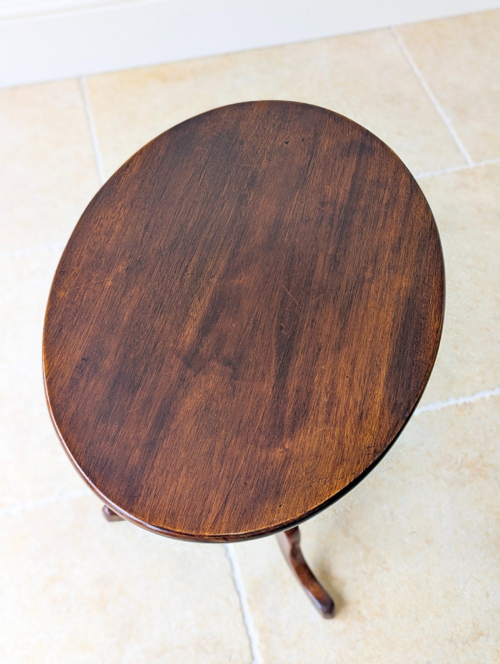 An antique Georgian mahogany wine table featuring a smooth oval top, turned central column, and three cabriole tripod legs. View III