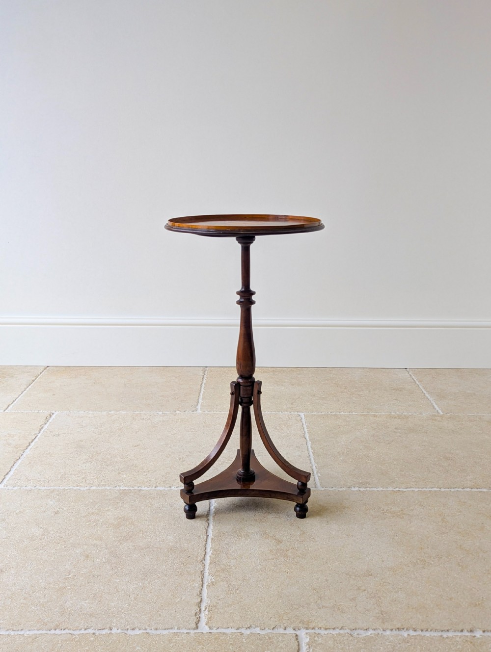 An Edwardian mahogany wine table featuring a circular top with a raised moulded edge, supported by a turned pedestal column and a triform base on small bun feet.