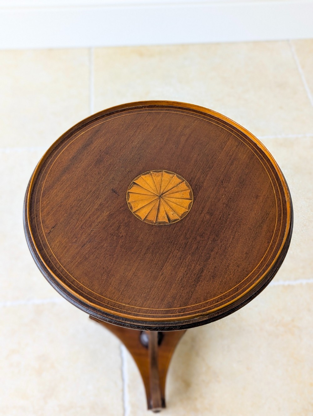 An Edwardian mahogany wine table featuring a circular top with a raised moulded edge, supported by a turned pedestal column and a triform base on small bun feet. View II