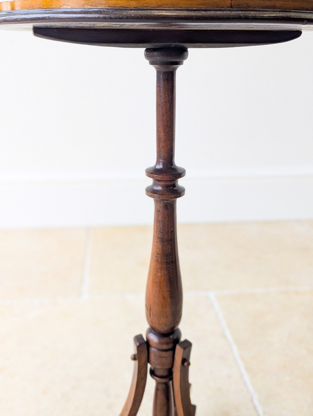 An Edwardian mahogany wine table featuring a circular top with a raised moulded edge, supported by a turned pedestal column and a triform base on small bun feet. View IV