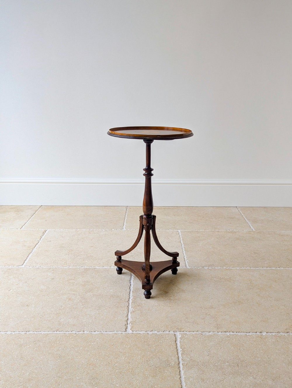 An Edwardian mahogany wine table featuring a circular top with a raised moulded edge, supported by a turned pedestal column and a triform base on small bun feet. View V