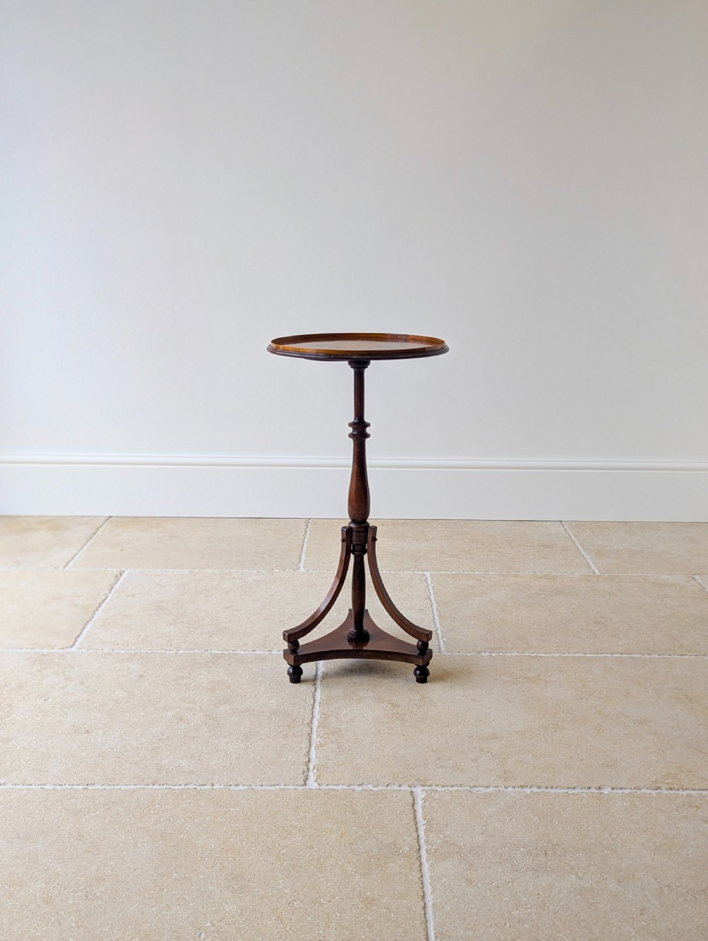 An Edwardian mahogany wine table featuring a circular top with a raised moulded edge, supported by a turned pedestal column and a triform base on small bun feet. View IX