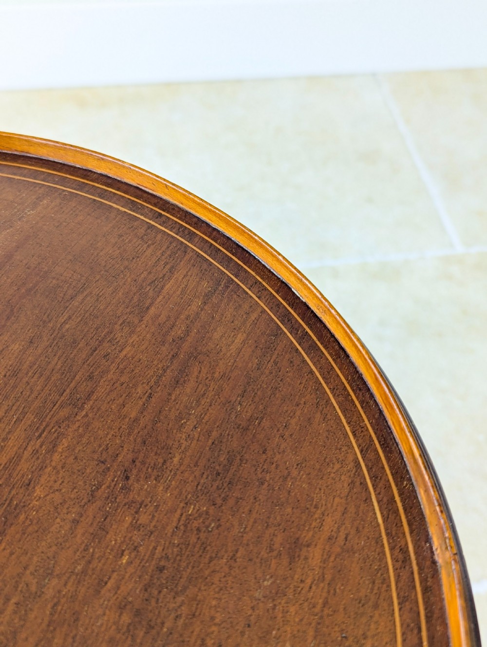 An Edwardian mahogany wine table featuring a circular top with a raised moulded edge, supported by a turned pedestal column and a triform base on small bun feet. View X