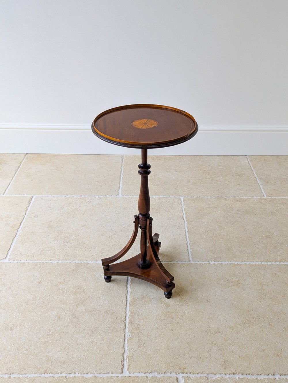 An Edwardian mahogany wine table featuring a circular top with a raised moulded edge, supported by a turned pedestal column and a triform base on small bun feet. View XII