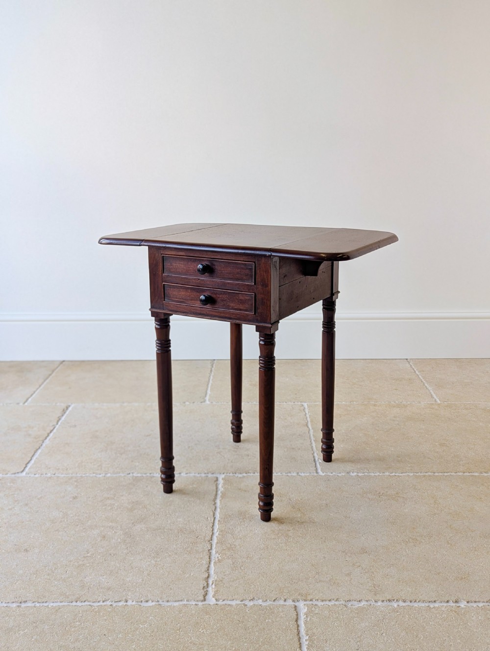An early Victorian dark mahogany Pembroke work table with two drawers, turned legs, and two extended drop-leaf flaps.