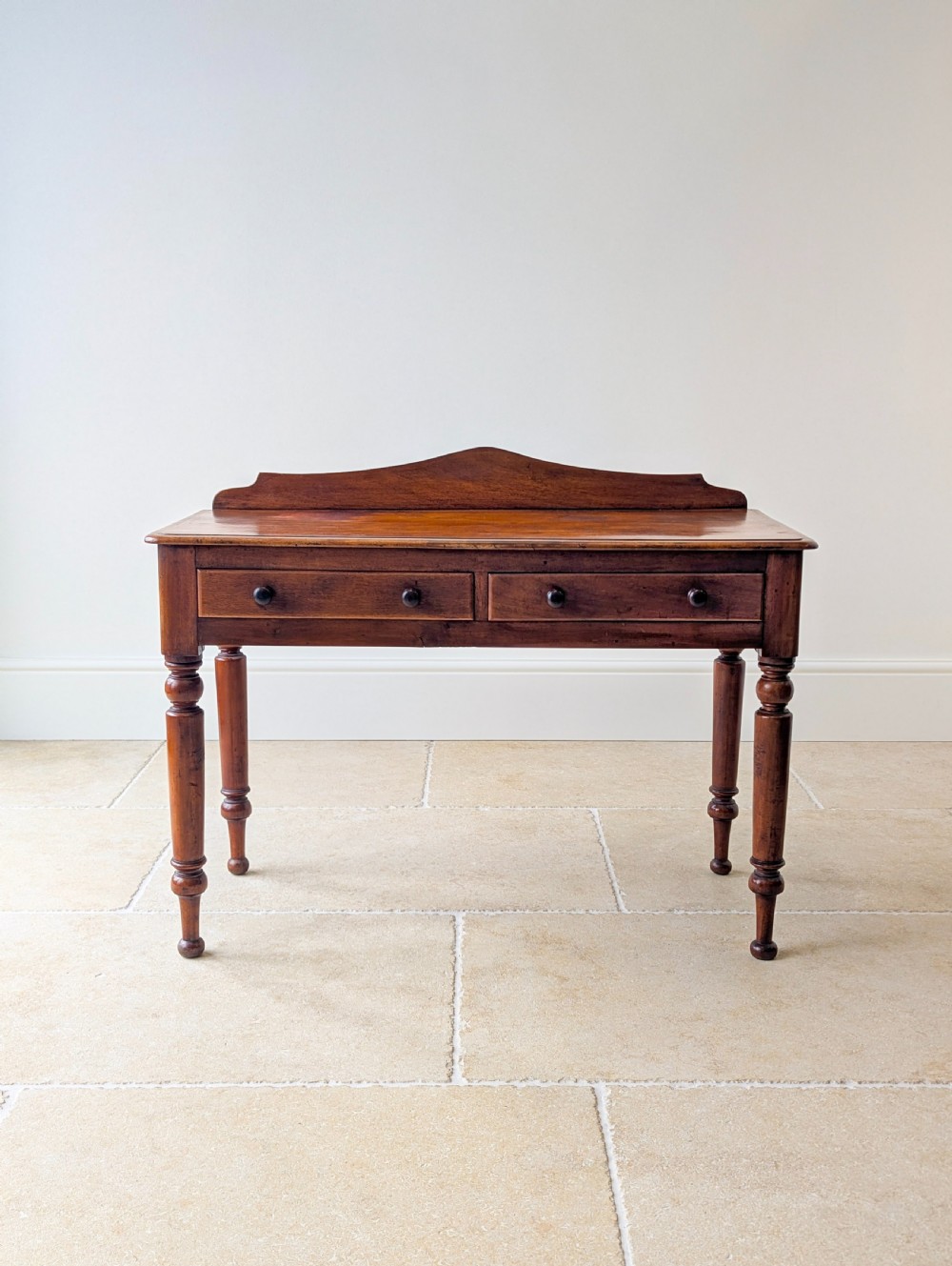 A Victorian mahogany writing table featuring two front drawers with dark turned knobs, a raised rear gallery upstand, and four turned legs. View II