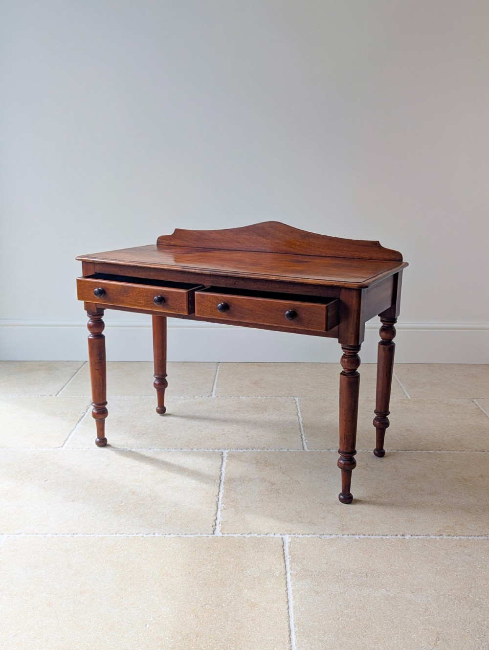 A Victorian mahogany writing table featuring two front drawers with dark turned knobs, a raised rear gallery upstand, and four turned legs. View III