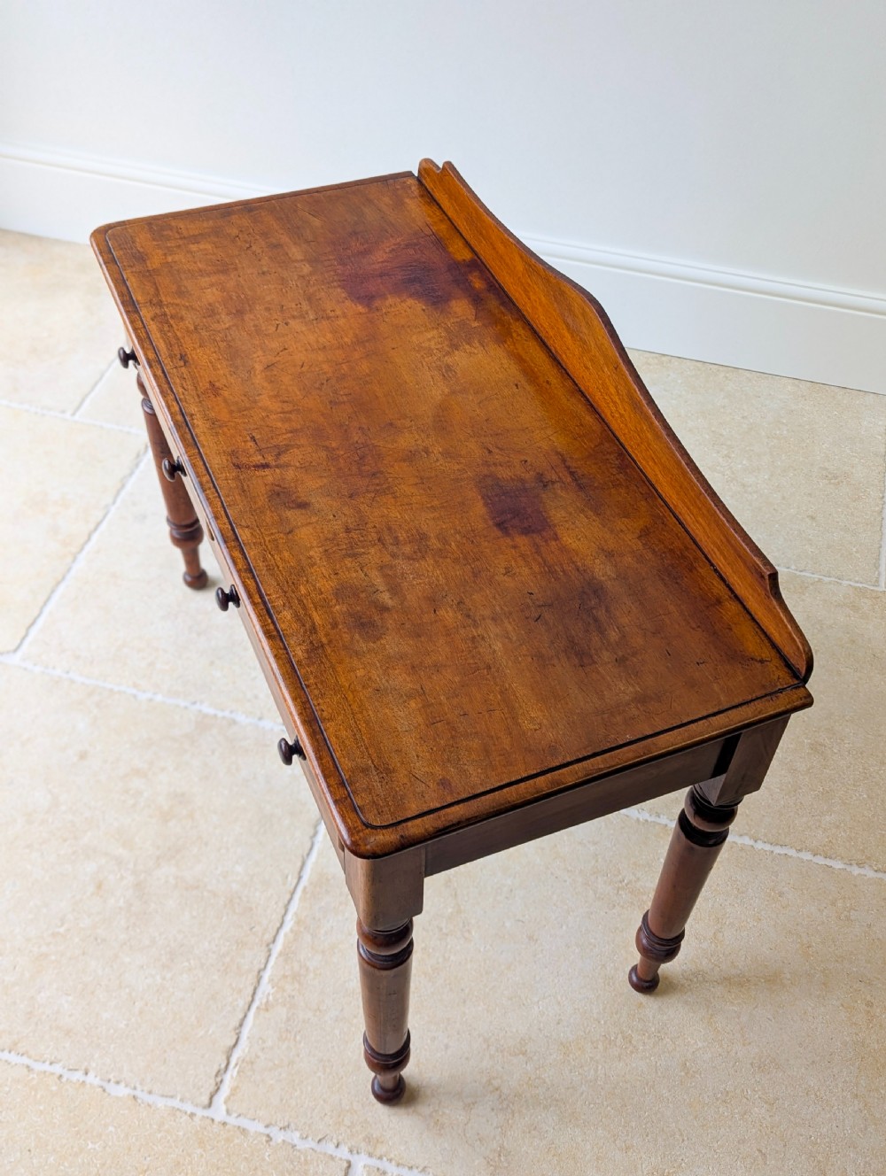 A Victorian mahogany writing table featuring two front drawers with dark turned knobs, a raised rear gallery upstand, and four turned legs. View IV
