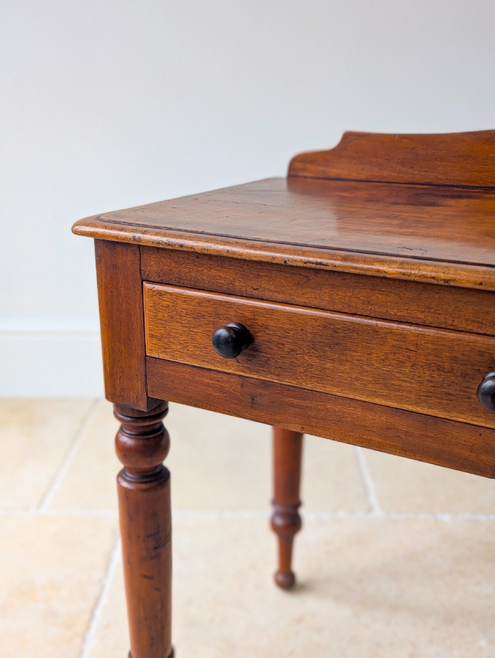 A Victorian mahogany writing table featuring two front drawers with dark turned knobs, a raised rear gallery upstand, and four turned legs. View V