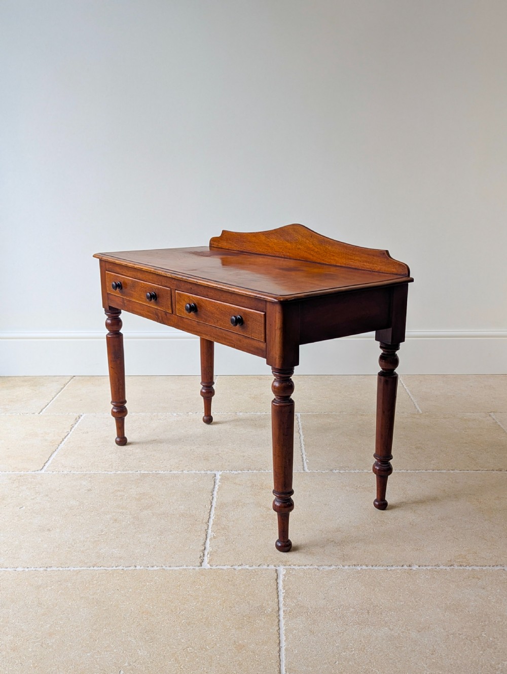 A Victorian mahogany writing table featuring two front drawers with dark turned knobs, a raised rear gallery upstand, and four turned legs. View VIII