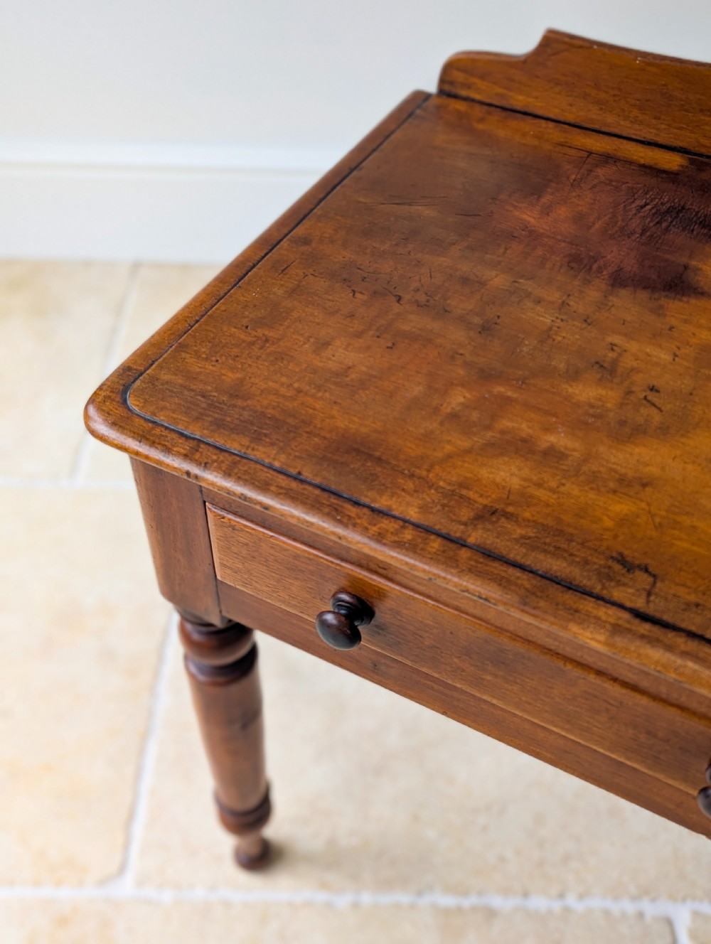 A Victorian mahogany writing table featuring two front drawers with dark turned knobs, a raised rear gallery upstand, and four turned legs. View X