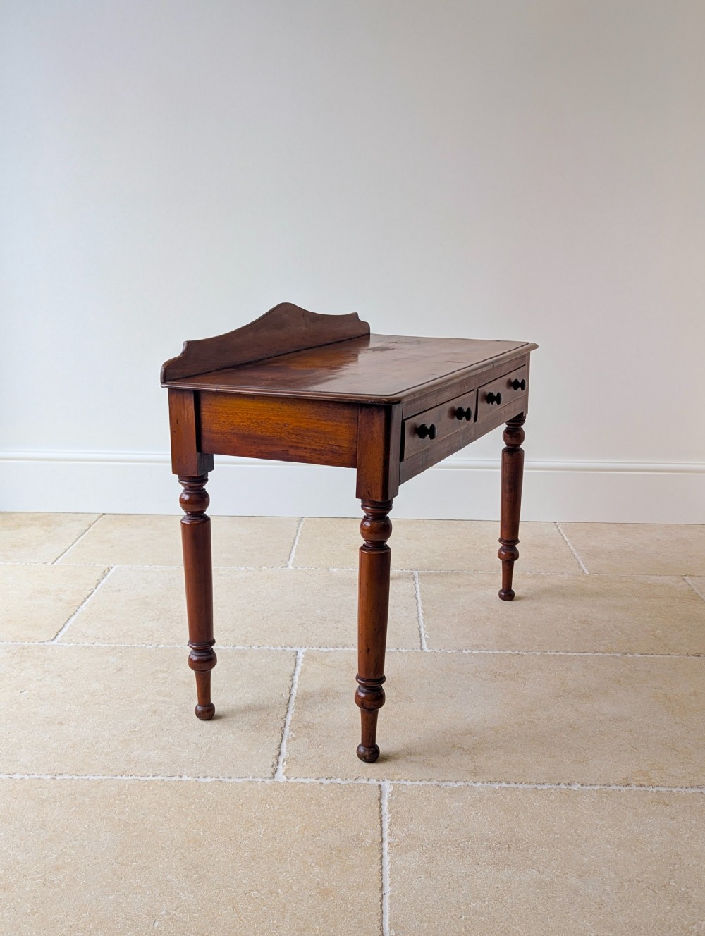 A Victorian mahogany writing table featuring two front drawers with dark turned knobs, a raised rear gallery upstand, and four turned legs. View XI