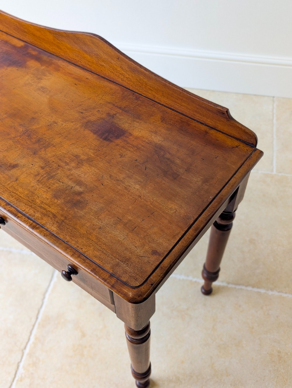 A Victorian mahogany writing table featuring two front drawers with dark turned knobs, a raised rear gallery upstand, and four turned legs. View XII