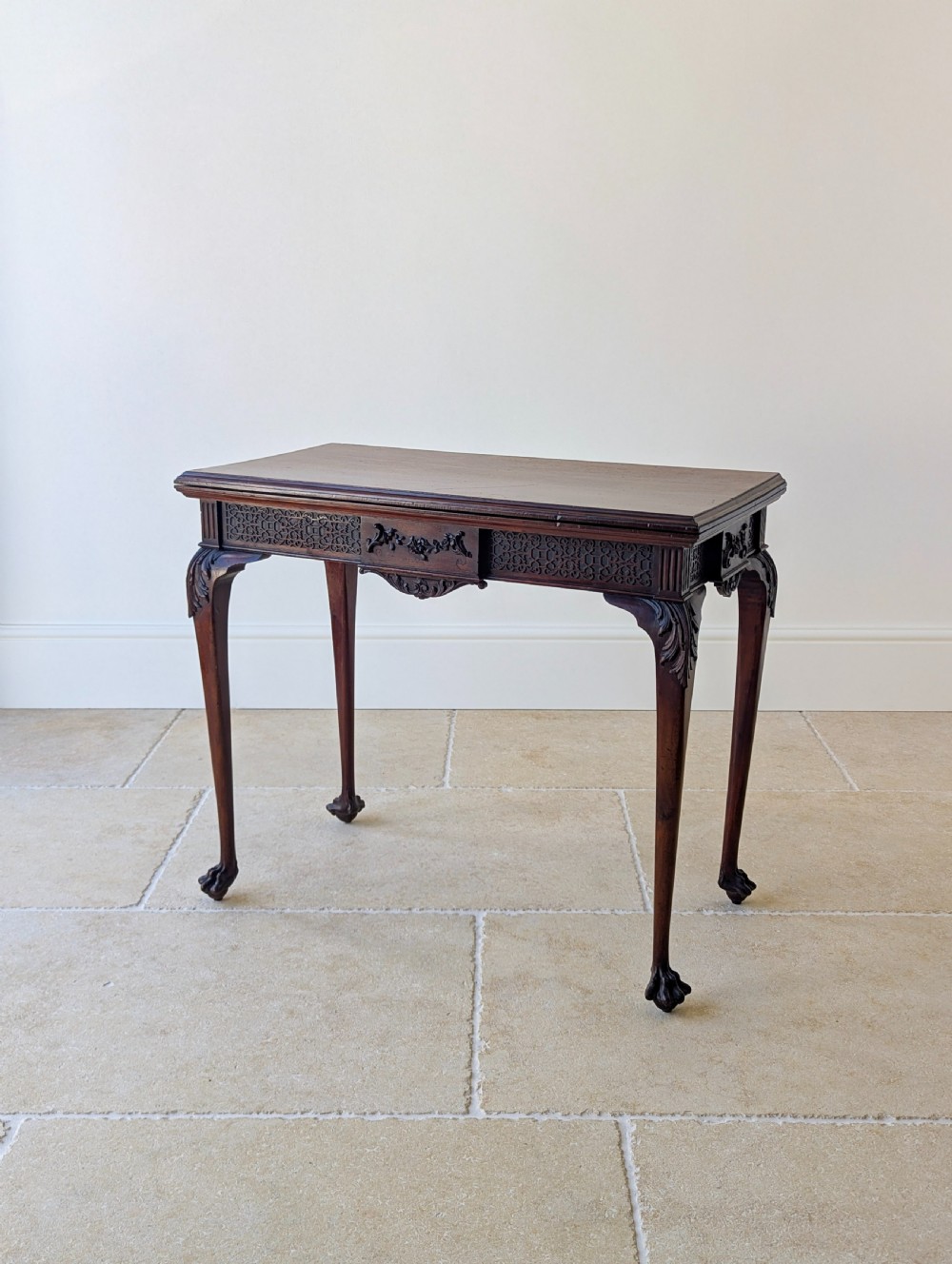 An Edwardian dark mahogany fold-over card table featuring carved cabriole legs, claw and ball feet, and blind fretwork along the apron.