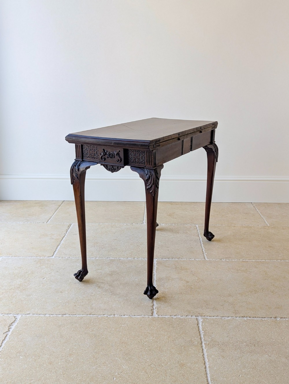 An Edwardian dark mahogany fold-over card table featuring carved cabriole legs, claw and ball feet, and blind fretwork along the apron. View XX