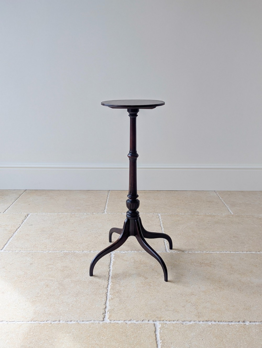 A tall, slender dark walnut torchere featuring a circular flat top, a turned central column, and a sweeping tripod base.