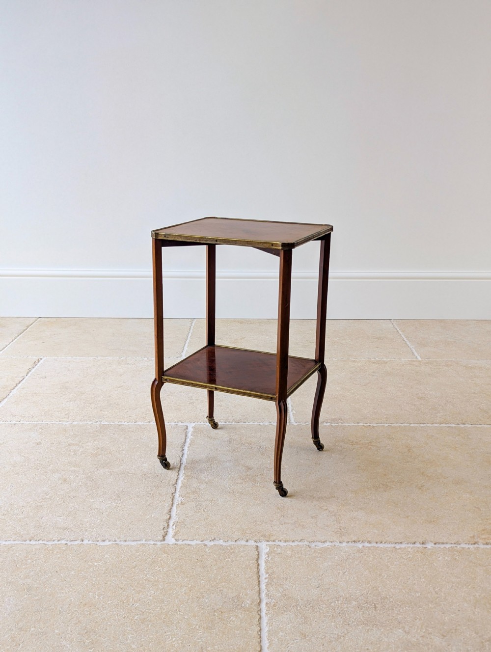 A late Victorian square mahogany two-tier occasional table with cabriole legs, brass-edged rims, and brass castors.