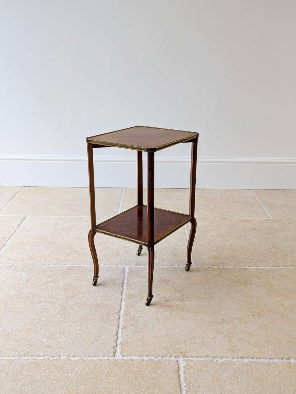 A late Victorian square mahogany two-tier occasional table with cabriole legs, brass-edged rims, and brass castors. View II