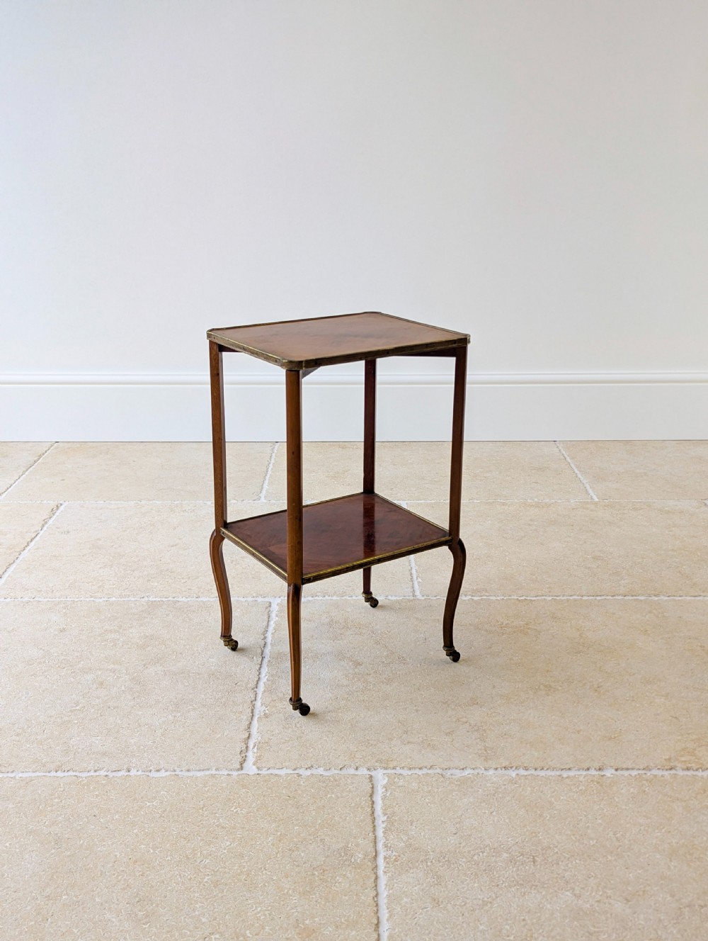 A late Victorian square mahogany two-tier occasional table with cabriole legs, brass-edged rims, and brass castors. View V