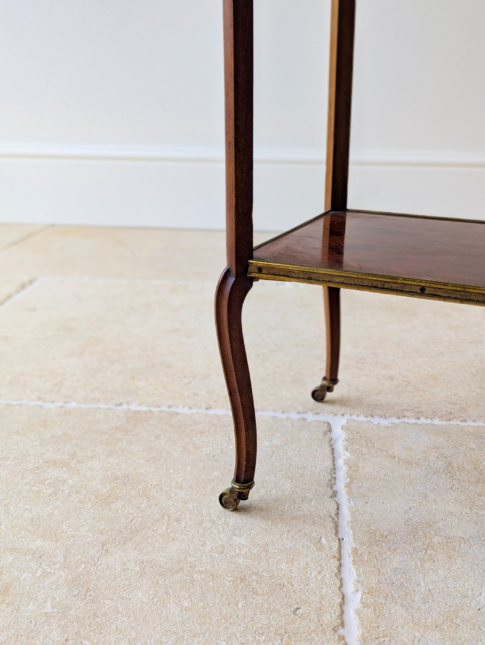 A late Victorian square mahogany two-tier occasional table with cabriole legs, brass-edged rims, and brass castors. View VII