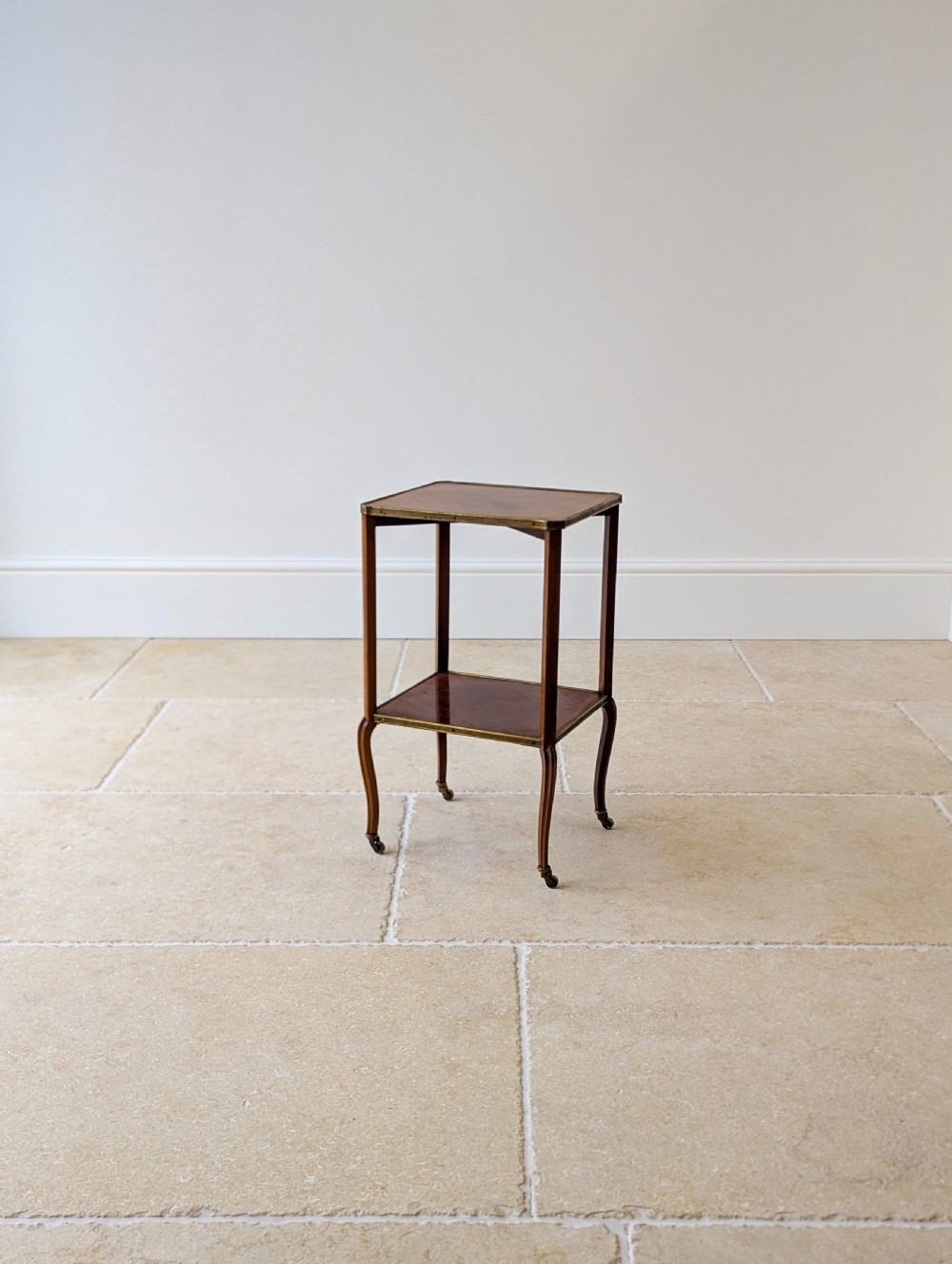 A late Victorian square mahogany two-tier occasional table with cabriole legs, brass-edged rims, and brass castors. View IX