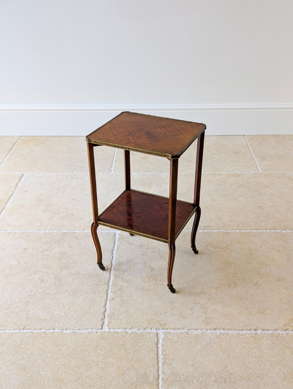 A late Victorian square mahogany two-tier occasional table with cabriole legs, brass-edged rims, and brass castors. View XVI