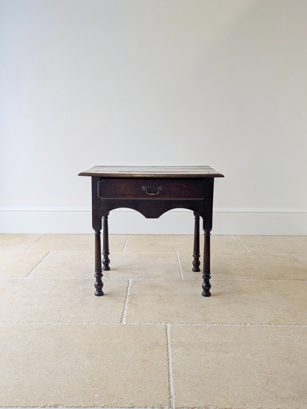 A dark oak Georgian lowboy featuring a single drawer with a brass drop handle, shaped frieze, and turned legs. View II