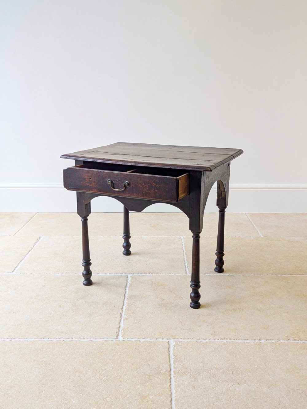 A dark oak Georgian lowboy featuring a single drawer with a brass drop handle, shaped frieze, and turned legs. View IV