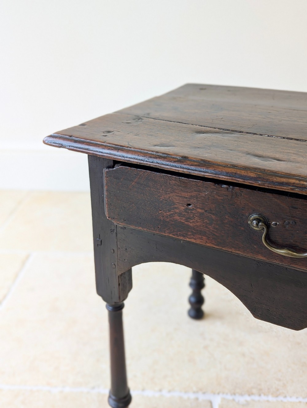 A dark oak Georgian lowboy featuring a single drawer with a brass drop handle, shaped frieze, and turned legs. View V