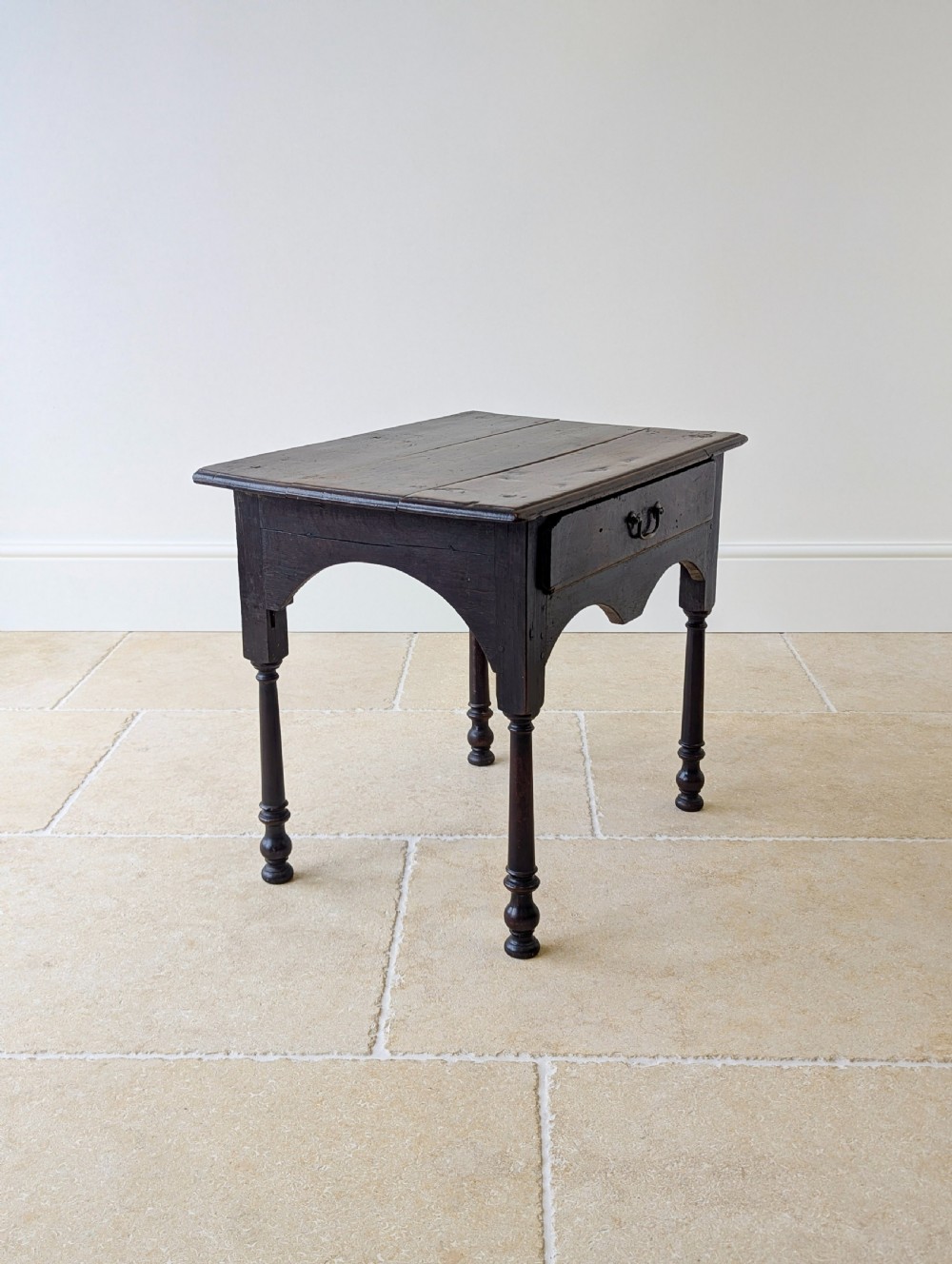 A dark oak Georgian lowboy featuring a single drawer with a brass drop handle, shaped frieze, and turned legs. View VI