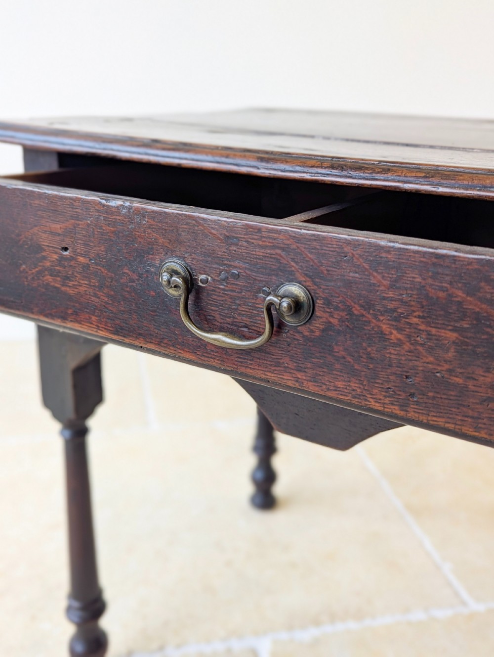 A dark oak Georgian lowboy featuring a single drawer with a brass drop handle, shaped frieze, and turned legs. View VII