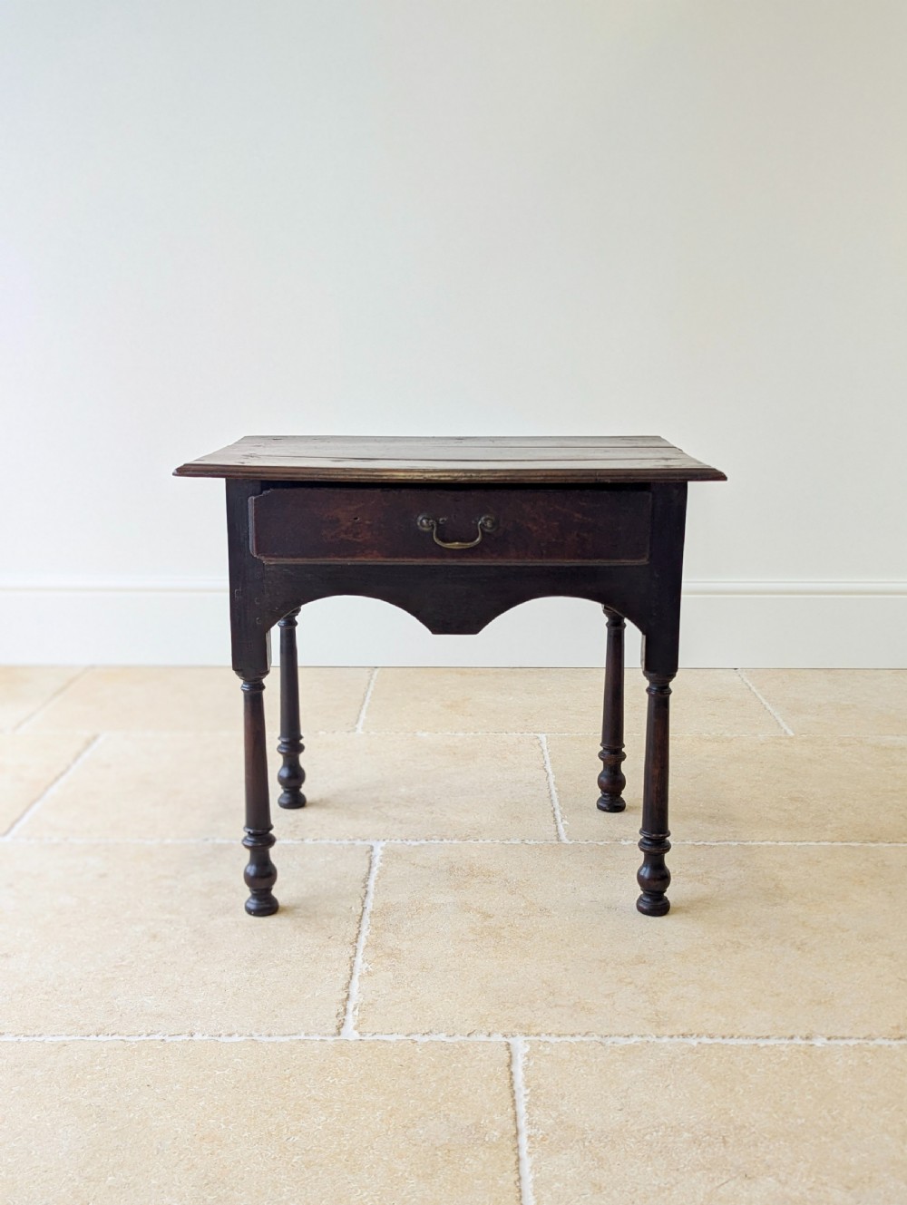 A dark oak Georgian lowboy featuring a single drawer with a brass drop handle, shaped frieze, and turned legs. View VIII