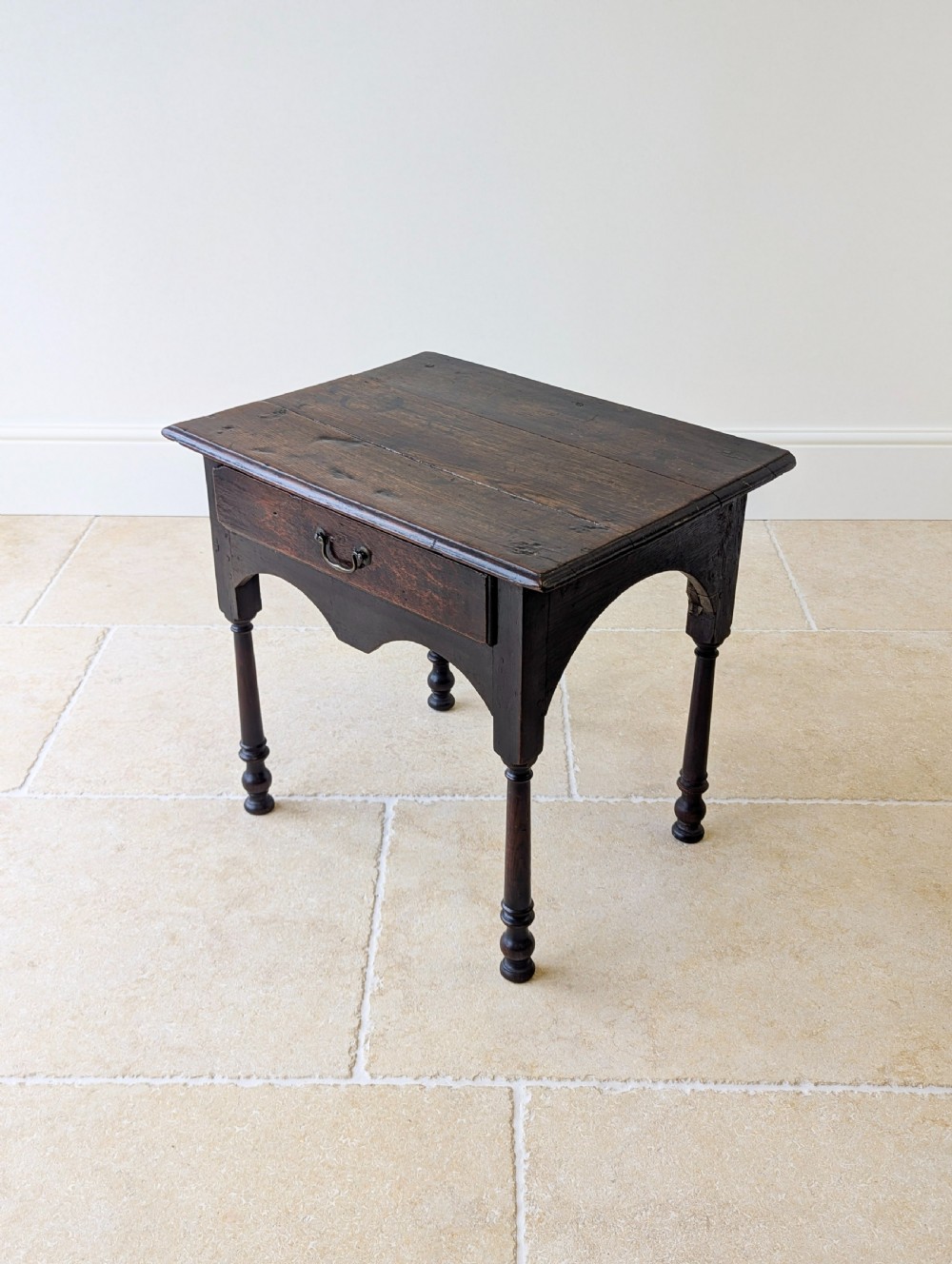 A dark oak Georgian lowboy featuring a single drawer with a brass drop handle, shaped frieze, and turned legs. View XI