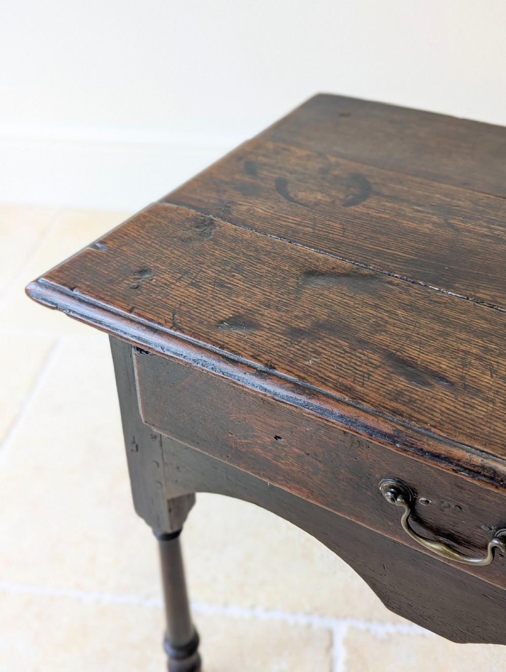 A dark oak Georgian lowboy featuring a single drawer with a brass drop handle, shaped frieze, and turned legs. View XII