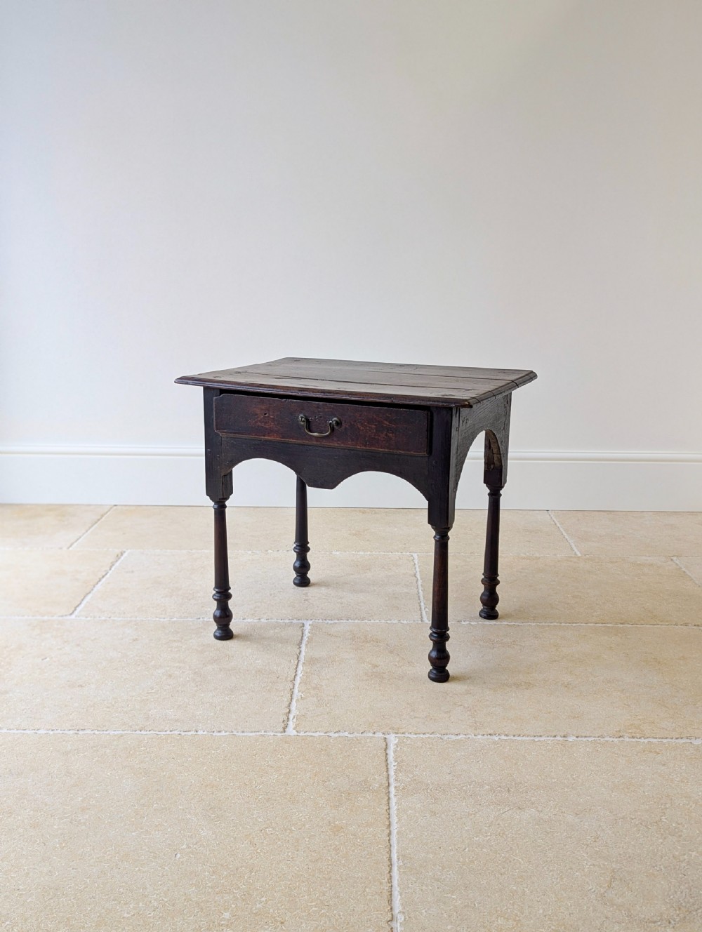 A dark oak Georgian lowboy featuring a single drawer with a brass drop handle, shaped frieze, and turned legs. View XIII