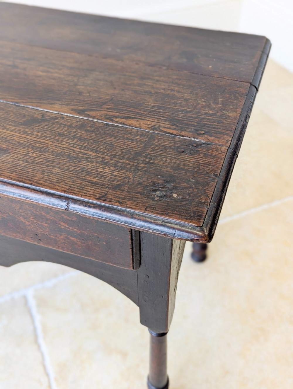 A dark oak Georgian lowboy featuring a single drawer with a brass drop handle, shaped frieze, and turned legs. View XVI