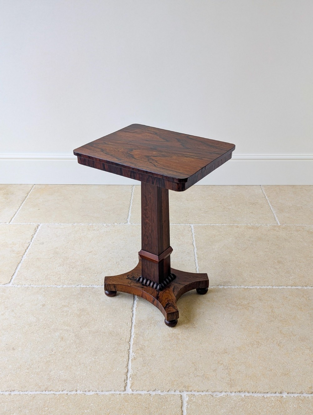 A Regency rosewood occasional table with a rectangular top, square column pedestal, and quadform base on compressed feet.