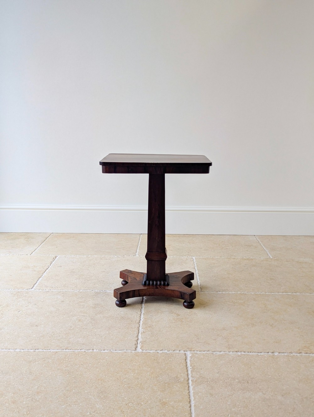 A Regency rosewood occasional table with a rectangular top, square column pedestal, and quadform base on compressed feet. View V