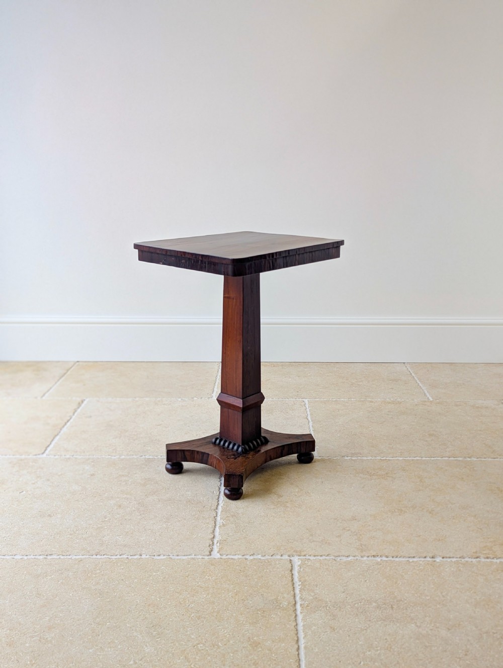 A Regency rosewood occasional table with a rectangular top, square column pedestal, and quadform base on compressed feet. View VII