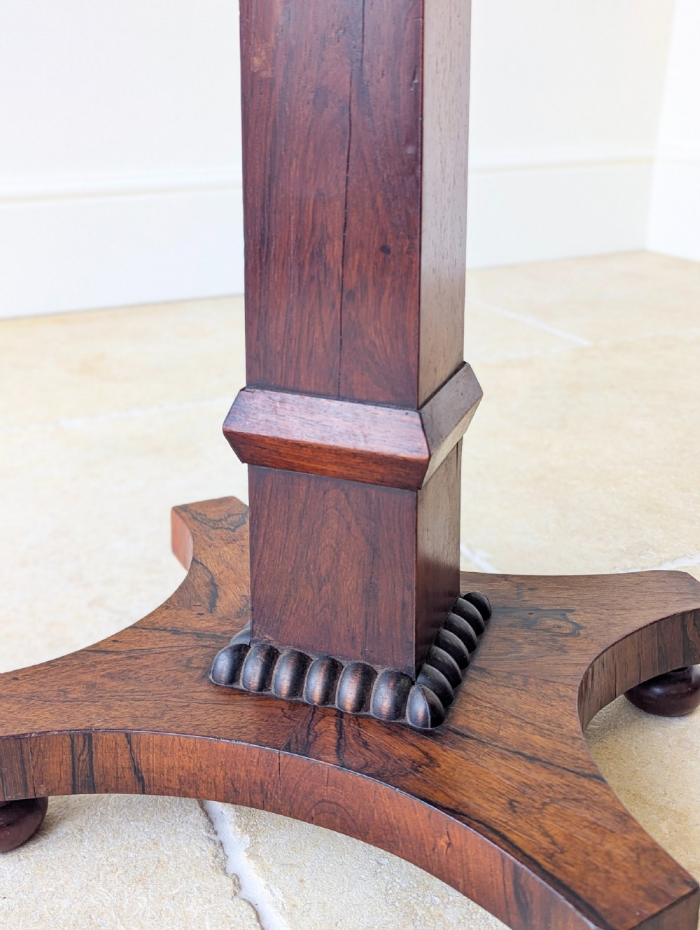 A Regency rosewood occasional table with a rectangular top, square column pedestal, and quadform base on compressed feet. View X