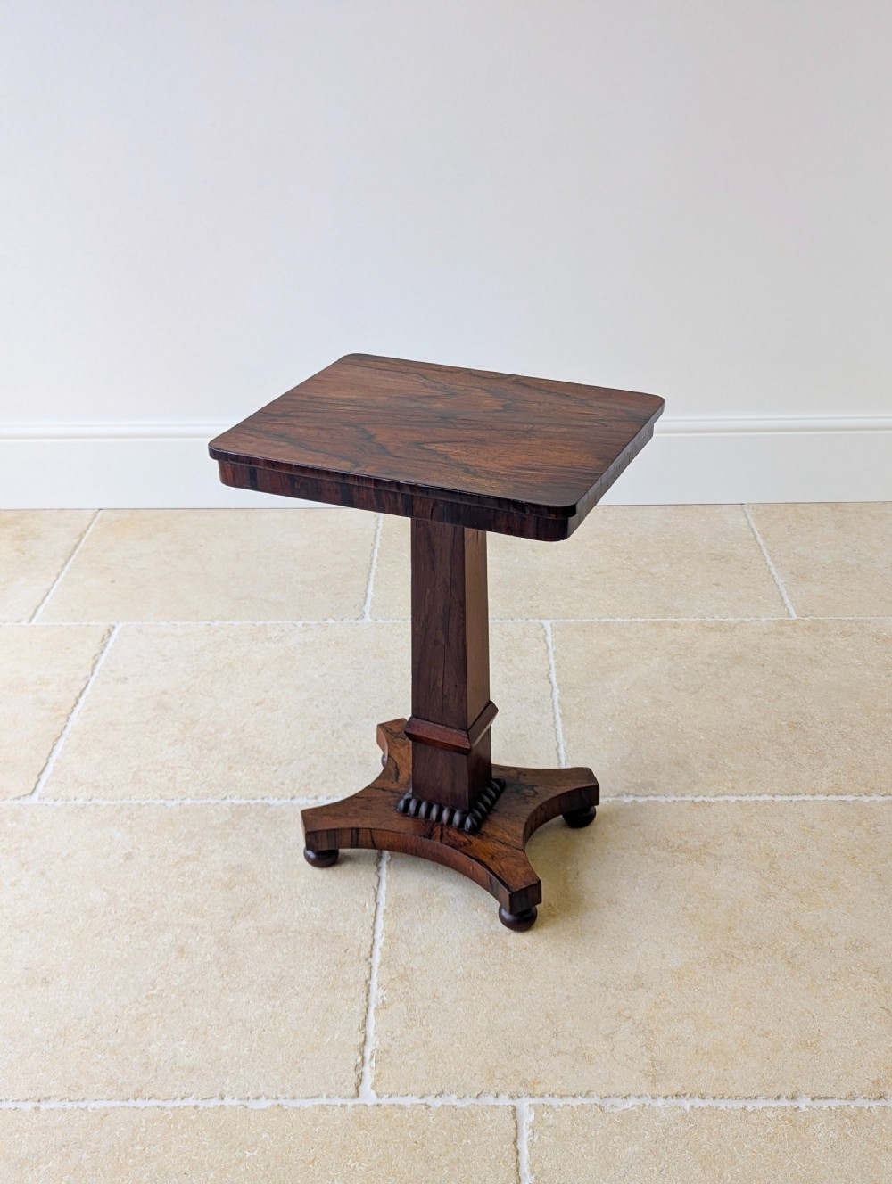 A Regency rosewood occasional table with a rectangular top, square column pedestal, and quadform base on compressed feet. View XVI