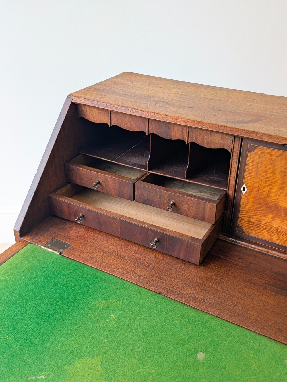 An antique Georgian mahogany slant-front bureau featuring four graduated long drawers with brass oval drop handles and shaped bracket feet. View XVII