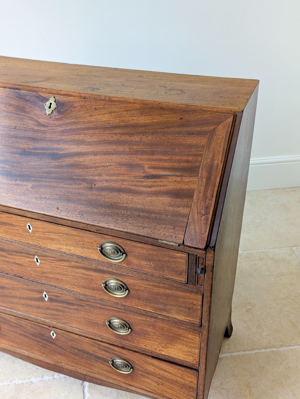 An antique Georgian mahogany slant-front bureau featuring four graduated long drawers with brass oval drop handles and shaped bracket feet. View XVIII