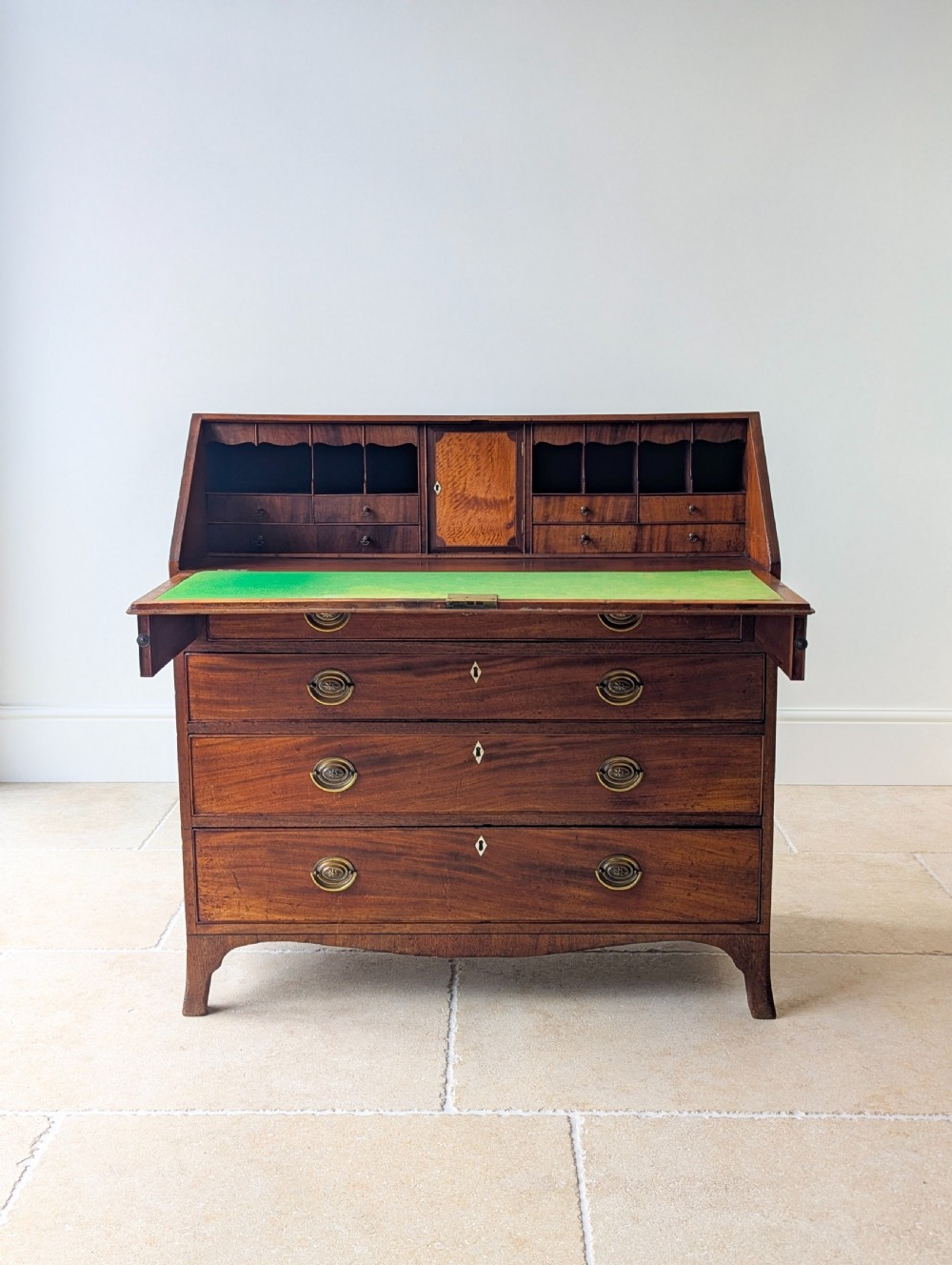 An antique Georgian mahogany slant-front bureau featuring four graduated long drawers with brass oval drop handles and shaped bracket feet. View II